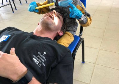 A young child sitting on a man s lap while he receives dental treatment from a dentist, with a small tool being used on his teeth.