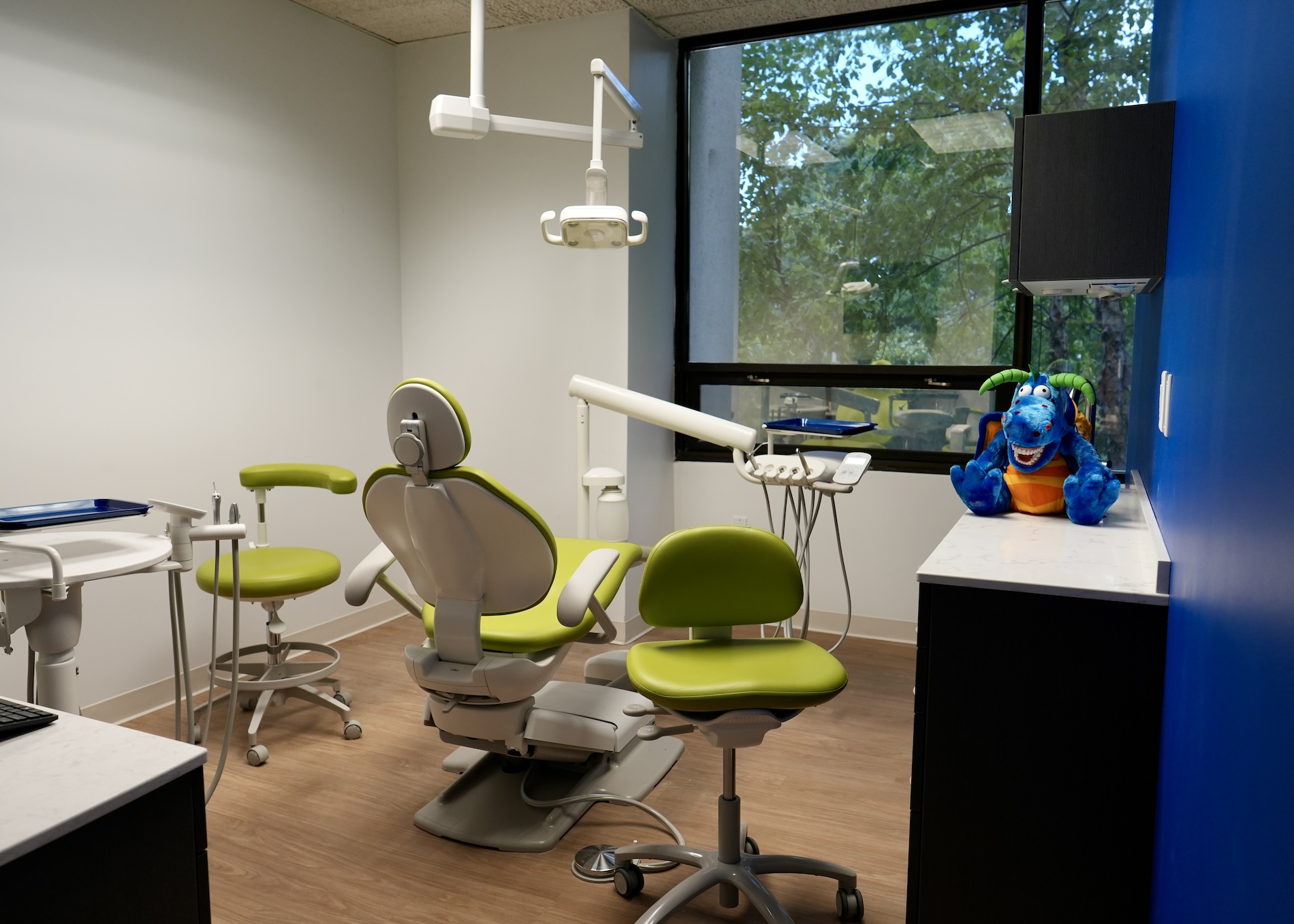 The image shows an interior view of a dental office with chairs, a desk, and various dental equipment.
