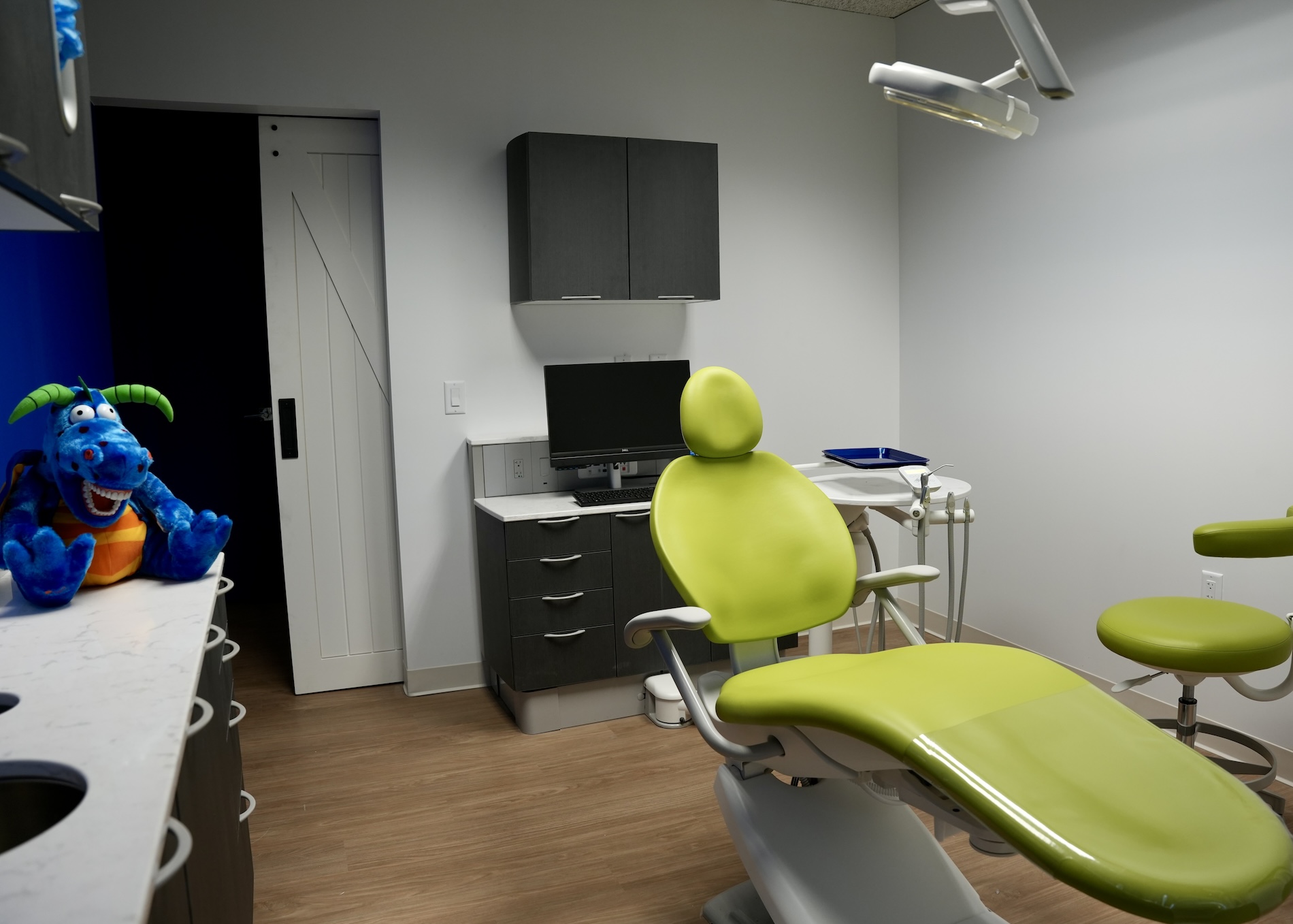 Dental office with a playful blue dinosaur character and a person standing in front of a dental chair.