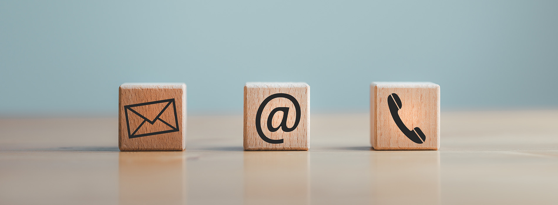 The image shows a collection of four wooden blocks with different symbols on them  an envelope, a phone, a call button, and a message icon, arranged in a row against a blurred background that appears to be a blue wall.