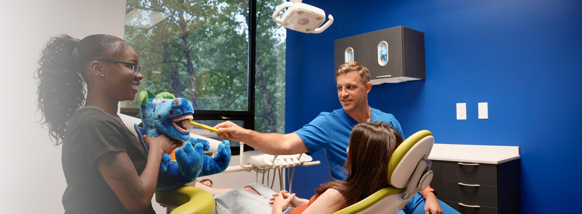 An image featuring a dental office setting with a dentist and two patients, one adult and one child, engaging in conversation while seated in chairs.