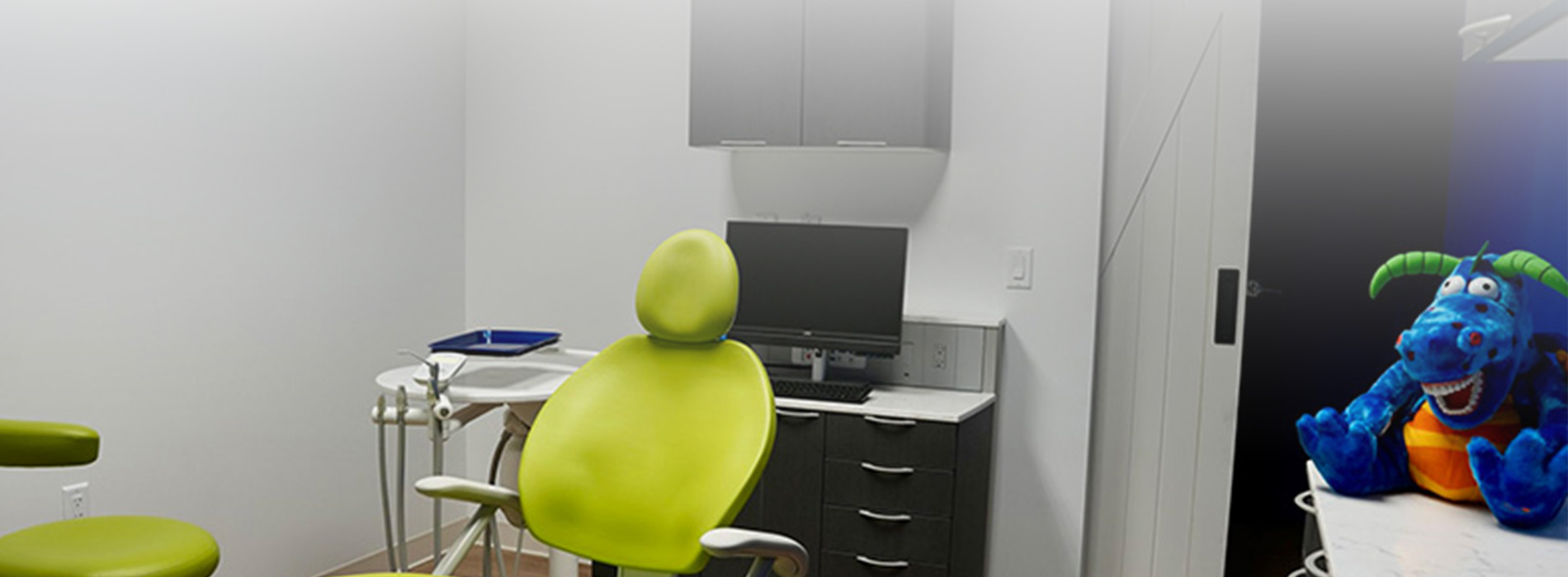 The image depicts a modern dental office with a blue color scheme, featuring a reception area with chairs, a desk, and a computer monitor.