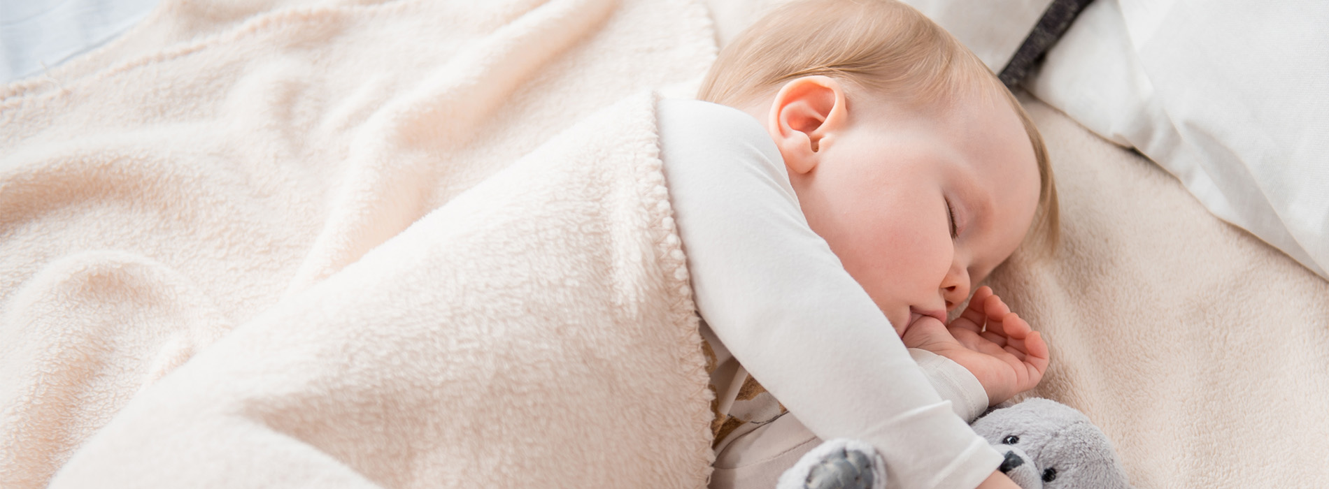 A baby sleeping peacefully on a bed with a blanket.